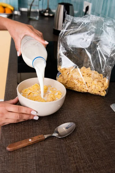 Vista ritagliata di donna afro-americana versando latte in ciotola con cornflakes — Foto stock