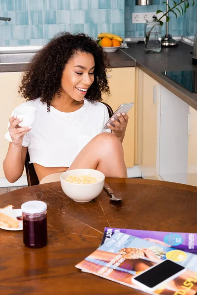 Feliz africana americana mujer usando smartphone cerca sabroso desayuno - foto de stock