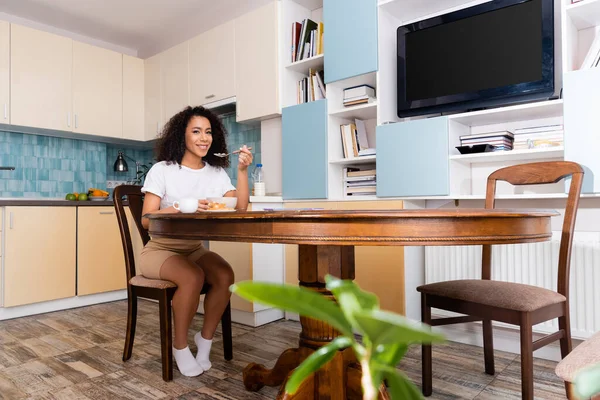 Feliz africano americano mujer sonriendo cerca sabroso desayuno en mesa - foto de stock