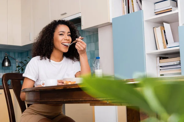 Glücklich afrikanisch-amerikanische Frau isst leckeres Frühstück in der Nähe von Tasse Kaffee — Stockfoto