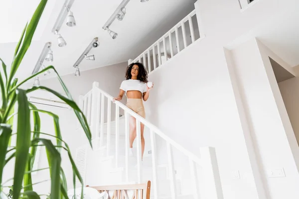 Selektiver Fokus einer jungen afrikanisch-amerikanischen Frau, die mit einer Tasse die Treppe hinuntergeht — Stockfoto