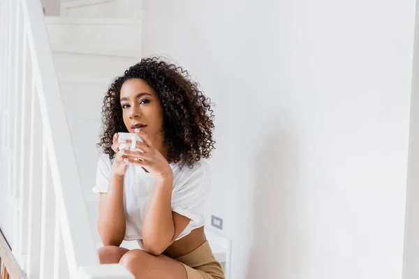 Atractiva mujer afroamericana sosteniendo taza de café - foto de stock