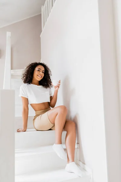 Glückliche afrikanisch-amerikanische Frau sitzt mit einer Tasse Kaffee auf einer Treppe — Stockfoto