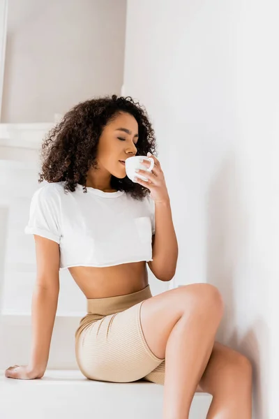 Young african american woman sitting on stairs and drinking coffee — Stock Photo