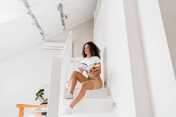 Jeune femme afro-américaine assis sur les escaliers avec magazine — Photo de stock