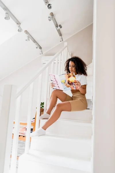 Молодая африканская американка сидит на лестнице и читает журнал — стоковое фото
