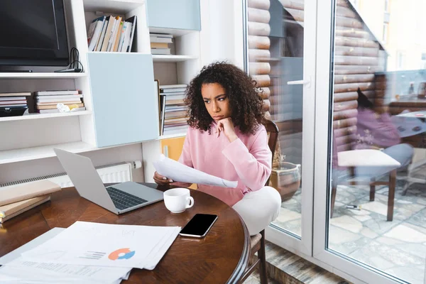 Pensoso afroamericano freelance in possesso di documenti vicino gadget e coppa — Foto stock