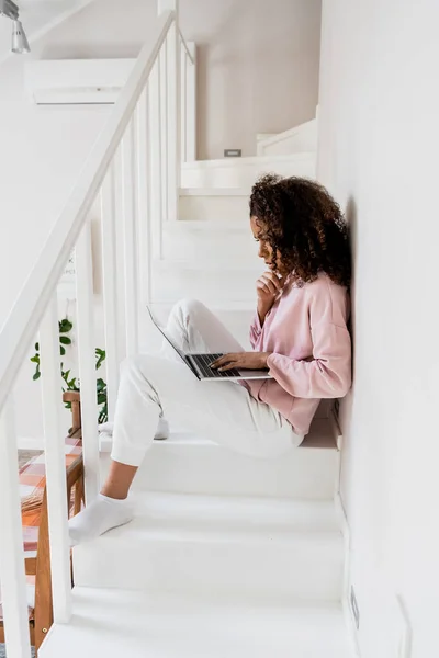 Focused african american freelancer sitting on stairs and using laptop — Stock Photo