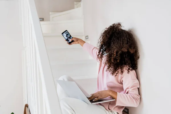 Curly african american freelancer sitting on stairs and taking selfie near laptop — Stock Photo