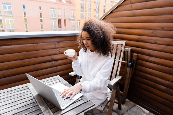 Curly african american freelancer holding cup and working outside — Stock Photo