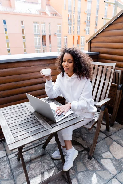 Rizado afroamericano freelancer celebración taza con café y trabajando fuera - foto de stock