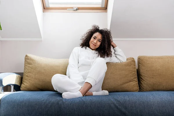 Jeune femme afro-américaine souriant assis sur le canapé — Photo de stock