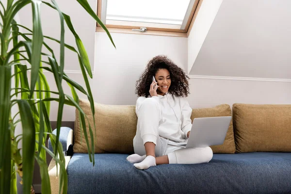 Selective focus of happy young african american freelancer talking on smartphone near laptop — Stock Photo