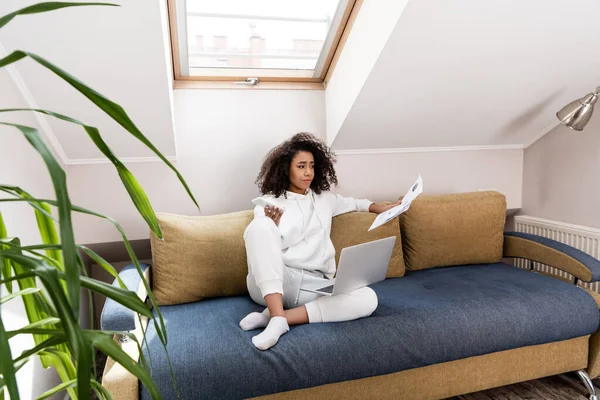 Selektiver Fokus junger afrikanisch-amerikanischer Freiberufler mit Smartphone und Blick auf Dokumente in Laptopnähe — Stockfoto