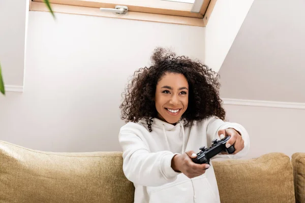КИЕВ, УКРАИНА - 15 апреля 2020 года: счастливая африканская американская девушка играет в видеоигры дома — стоковое фото