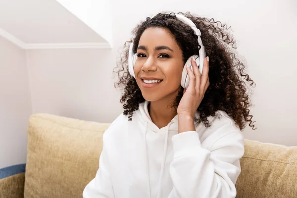 Chica afroamericana feliz en auriculares inalámbricos escuchando música en casa - foto de stock