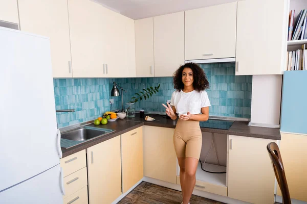 Cheerful african american girl holding cup and showing peace sign near fresh fruits — Stock Photo