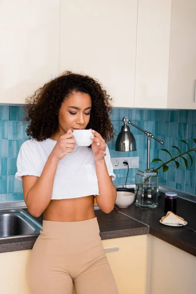 Curly african american girl drinking coffee while holding cup — Stock Photo