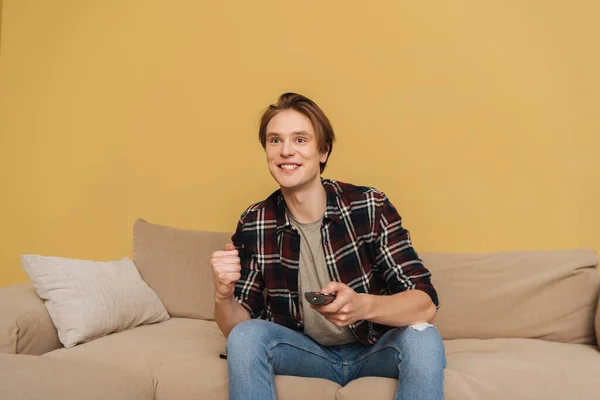 Positive man sitting on sofa and holding remote controller, end of quarantine concept — Stock Photo