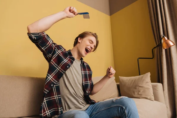 Cheerful man with closed eyes sitting on sofa and holding passport with air ticket, end of quarantine concept — Stock Photo