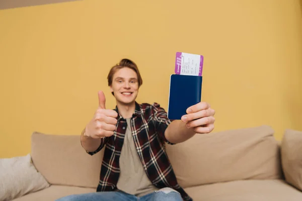 Selective focus of cheerful man showing thumb up and holding passport with air ticket, end of quarantine concept — Stock Photo