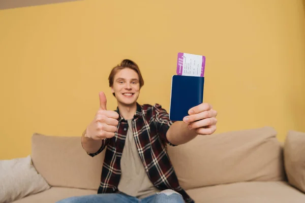 Enfoque selectivo del hombre alegre mostrando el pulgar hacia arriba y la celebración de pasaporte con billete de avión, fin del concepto de cuarentena - foto de stock