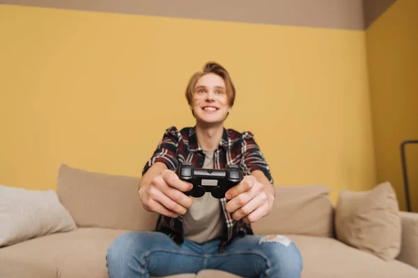 KYIV, UKRAINE - APRIL 24, 2020: selective focus of cheerful man holding joystick while playing video game in living room — Stock Photo