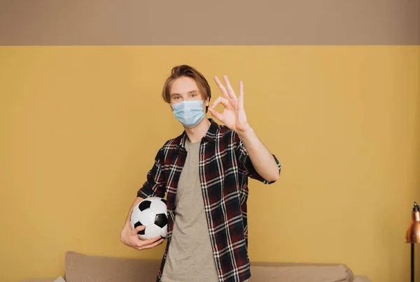 Mann mit medizinischer Maske hält Fußball in der Hand und zeigt Okay-Zeichen, Ende der Quarantäne — Stockfoto