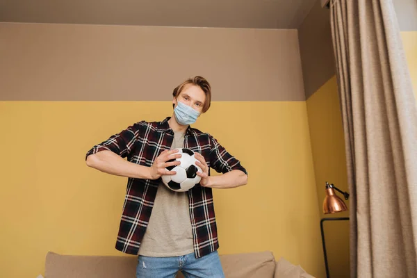 Homme en masque médical tenant le football et regardant la caméra, fin du concept de quarantaine — Photo de stock