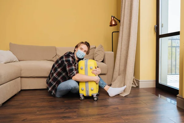 Man in medical mask sitting on floor and touching baggage, end of quarantine concept — Stock Photo