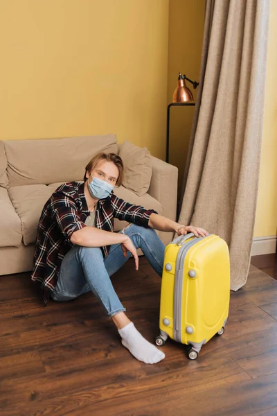 Young man in medical mask sitting on floor near baggage, end of quarantine concept — Stock Photo