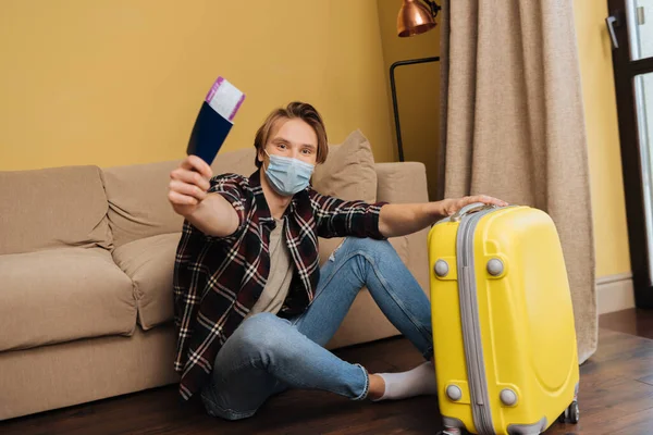 Homem em máscara médica segurando passaporte com bilhete de ar perto da bagagem, fim do conceito de quarentena — Fotografia de Stock