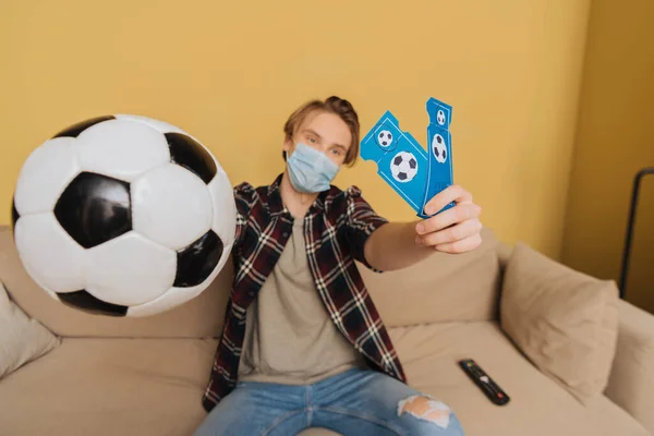 Selective focus of man in medical mask holding football and sport match tickets, end of quarantine concept — Stock Photo