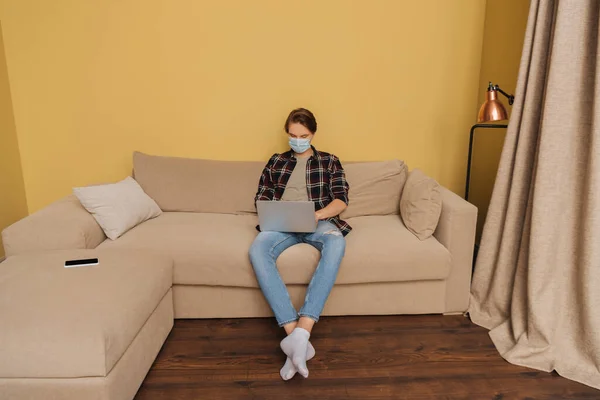 Freelancer in medical mask using laptop near smartphone with blank screen — Stock Photo