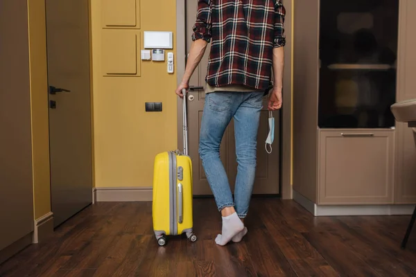 Vista recortada del hombre sosteniendo máscara médica y caminando con equipaje, fin del concepto de cuarentena - foto de stock