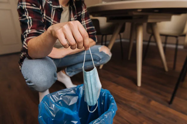 Vista recortada del joven lanzando máscara médica en el bote de basura con bolsa de basura, fin del concepto de cuarentena - foto de stock