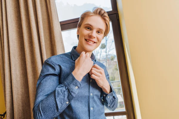 Joyeux jeune homme touchant chemise bleue à la maison, fin du concept de quarantaine — Photo de stock