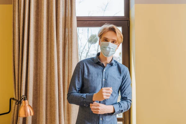 Junger Mann mit medizinischer Maske schaut zu Hause in die Kamera — Stockfoto