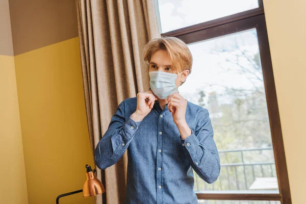 Joven tocando máscara médica en casa - foto de stock