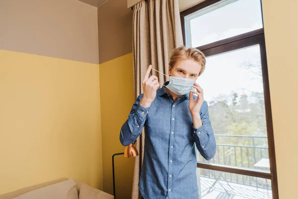 Joven con máscara médica azul en casa - foto de stock