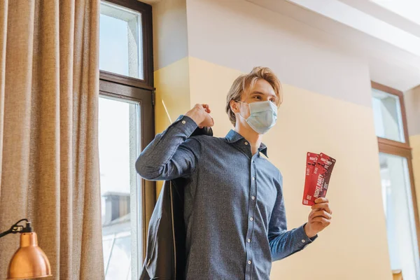 Stylish man in medical mask holding night party tickets and jacket, end of quarantine concept — Stock Photo