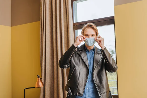 Hombre con chaqueta tocando máscara médica en casa, fin del concepto de cuarentena - foto de stock