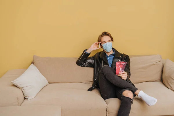 Stilvoller Mann mit medizinischer Maske und Jacke, der nächtliche Party-Tickets in der Hand hält und mit dem Smartphone spricht, Ende der Quarantäne — Stockfoto