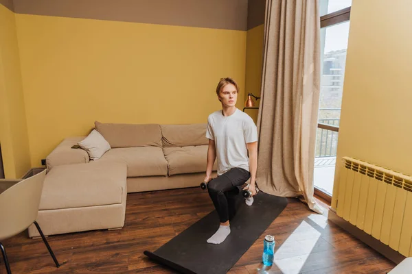 Young man exercising with dumbbells on fitness mat, end of quarantine concept — Stock Photo