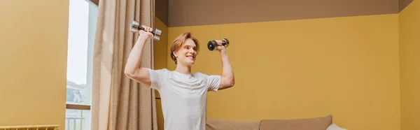 Panoramic crop of happy young man exercising with dumbbells in living room, end of quarantine concept — Stock Photo