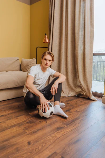 Handsome man holding football while sitting on floor, end of quarantine concept — Stock Photo
