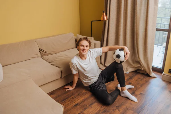 Felice uomo in possesso di calcio mentre seduto sul pavimento, fine del concetto di quarantena — Foto stock