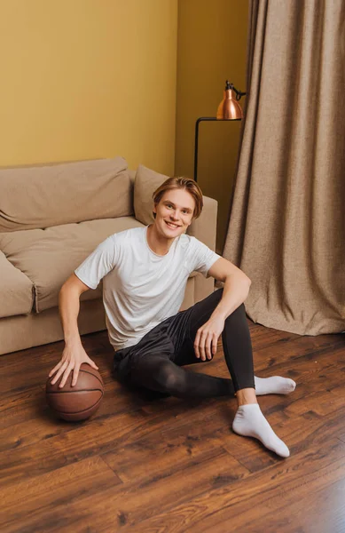 Счастливый человек, держащий баскетбол сидя на полу, конец концепции карантина — стоковое фото