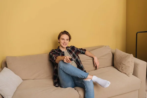 Feliz hombre sosteniendo mando a distancia y sentado en el sofá, fin del concepto de cuarentena - foto de stock