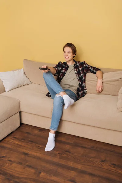 Cheerful man holding remote controller and sitting on sofa, end of quarantine concept — Stock Photo